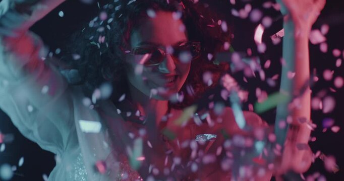 Happy young woman throwing confetti and dancing having fun in neon light on dark background. Entertainment and festive mood concept.