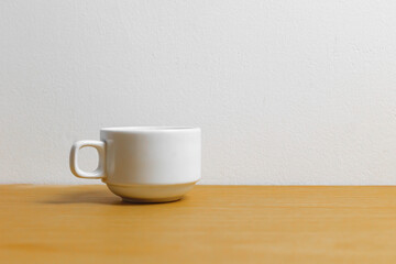 Simple white ceramic mug on wooden table against plain wall