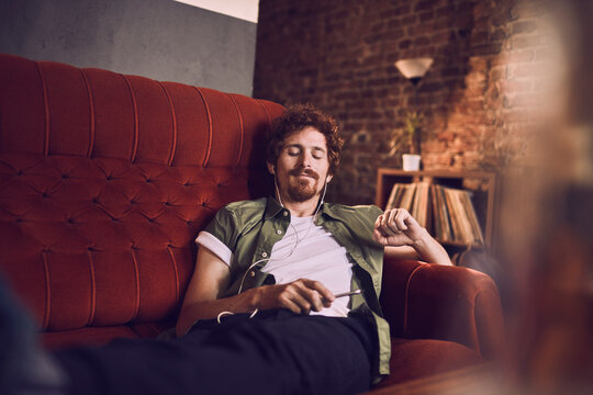 Man relaxing on couch with headphones and a smartphone in bar