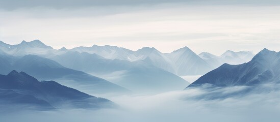 Fototapeta premium Serene blue Austrian mountain range under cloudy sky with soft mist enveloping the lower peaks creating a tranquil atmosphere and depth