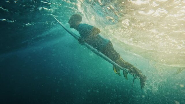Surfer riding waves while another surfer performing duck dive trick at sunset
