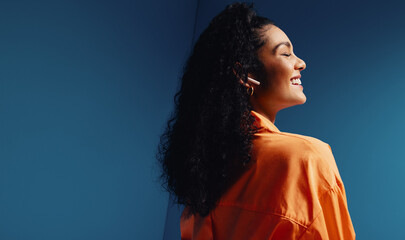 Woman listening to music with earphones in a vibrant, colorblocked studio, showing joyful and relaxed expressions