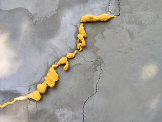 Winding crack in plastered concrete gray wall sealed with yellow construction foam. Temporary...