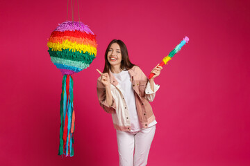 Happy woman with colorful pinata and stick on pink background