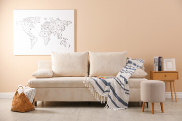 Comfortable sofa with pillows, blanket, pouf and picture indoors