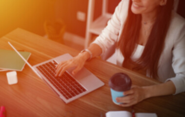 A blurred image of a woman working on a laptop in a cozy home office, holding a coffee cup in one...