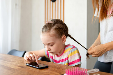 Little girl playing with smartphone while sitting at table in kitchen