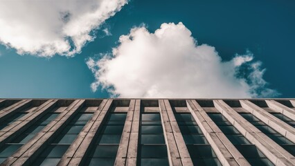 Fototapeta premium Reinforced concrete building facade under a clear blue sky with fluffy white clouds contrasting with the horizontal lines of the structure.