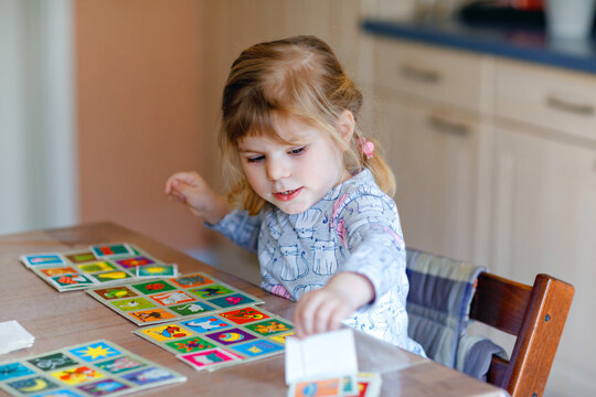 Excited smiling cute toddler girl playing picture card game. Happy healthy child training memory, thinking. Creative indoors leisure and education of kid. Family activity at home.