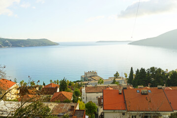 Aerial view of Savina area in Herceg Novi, Montenegro: landscape with entrance to Kotor Bay, calm Adriatic Sea, Plaža hotel, Lustica and Prevlaka peninsulas, red tiled roofs of residential buildings.