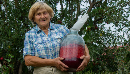 Elderly Woman Holding a Glass Bottle with Raspberries in the Garden © Anna