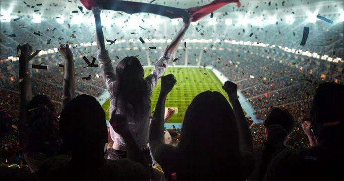 4K video of a lively stadium crowd at a nighttime soccer game, cheering with a large flag and confetti under bright lights