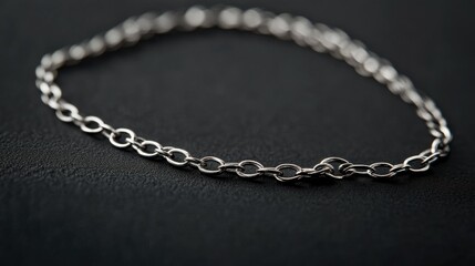 A minimalist display of a silver chain necklace on a dark black background, highlighting its craftsmanship