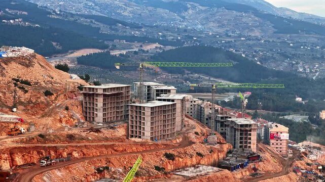The video shows a multi-story residential construction site. Buildings are at different stages; some in the rough construction phase. The site includes roads, material areas,situated on a hillside.