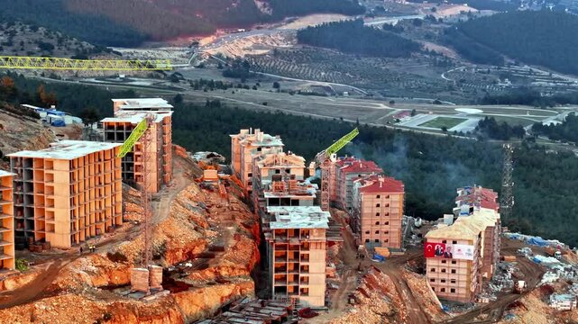 The video shows a multi-story residential construction site. Buildings are at different stages; some in the rough construction phase. The site includes roads, material areas,situated on a hillside.