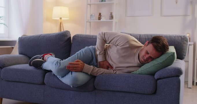 Sick man lying on sofa, touching belly in suffer from stomach ache, ill, struggles with bad pain, having eating disorder or indigestion trouble, health problem, appendicitis, abdomen tummy infection