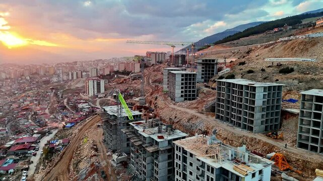 The video shows a multi-story residential construction site. Buildings are at different stages; some in the rough construction phase. The site includes roads, material areas,situated on a hillside.