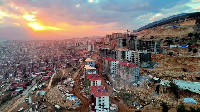 The video shows a multi-story residential construction site. Buildings are at different stages; some in the rough construction phase. The site includes roads, material areas,situated on a hillside.