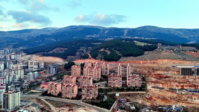 The video shows a multi-story residential construction site. Buildings are at different stages; some in the rough construction phase. The site includes roads, material areas,situated on a hillside.
