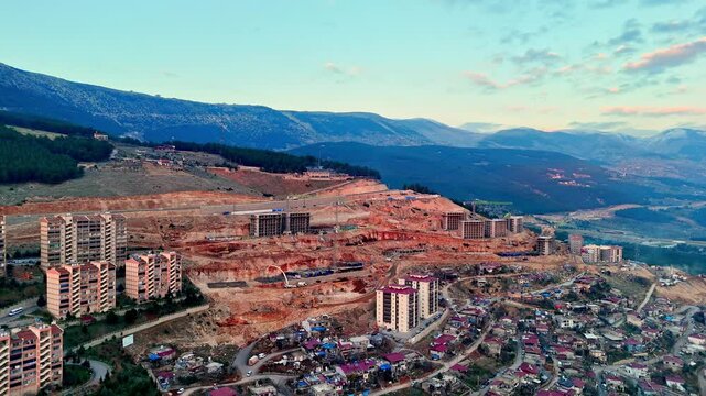 The video shows a multi-story residential construction site. Buildings are at different stages; some in the rough construction phase. The site includes roads, material areas,situated on a hillside.