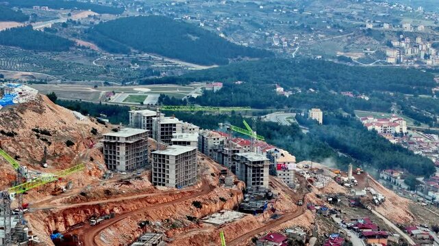 The video shows a multi-story residential construction site. Buildings are at different stages; some in the rough construction phase. The site includes roads, material areas,situated on a hillside.