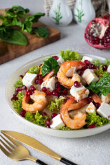 Salad with shrimps, pineapple, feta and pomegranate seeds in a plate on green lettuce leaves