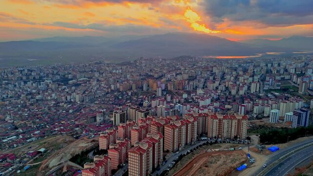 The video shows a wide cityscape at sunset with completed multi-story residential buildings in the foreground. The housing appears to be part of a large-scale residential construction project.