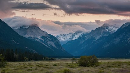 Breathtaking valley landscape showcasing majestic mountains draped in clouds with moody sunset hues and lush greenery in the foreground.