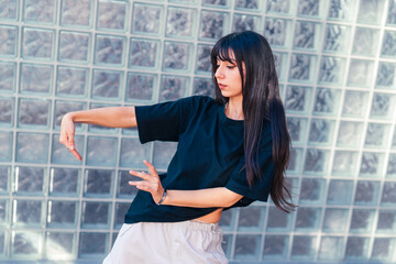 Young dancer performs expressive moves against a contemporary glass wall on a bright day