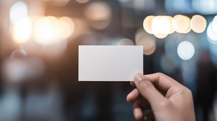 A hand holds a blank card against a blurred background of lights and people.