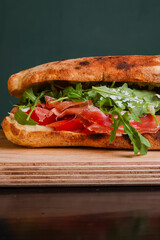 Panuozzo tradizionale napoletano ripieno di prosciutto crudo, rucola, scaglie di formaggio, mozzarella e pomodori freschi servito su un tagliere di legno