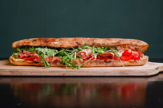 Panuozzo tradizionale napoletano ripieno di prosciutto crudo, rucola, scaglie di formaggio, mozzarella e pomodori freschi servito su un tagliere di legno