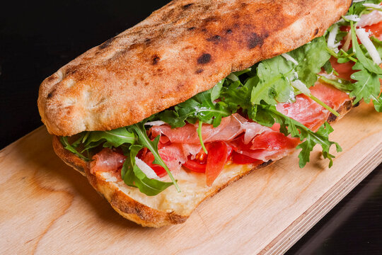 Panuozzo tradizionale napoletano ripieno di prosciutto crudo, rucola, scaglie di formaggio, mozzarella e pomodori freschi servito su un tagliere di legno