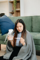 Fototapeta premium Young Asian woman suffering from flu symptoms, covered with a blanket on a sofa. Concept of illness, healthcare,