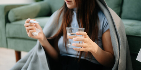 Young Asian woman suffering from flu symptoms, covered with a blanket on a sofa. Concept of illness, healthcare,