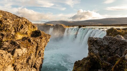 Scenic view of Godafoss waterfall cascading over rocky cliffs under a partly cloudy sky