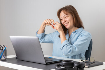 Smiling happy woman with laptop has a videocall meeting with friend or partner, shows love heart...