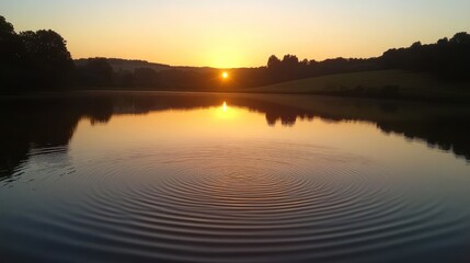 Fototapeta premium Sunset reflecting on calm lake water with concentric ripples