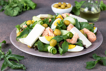 Salad with canned salmon, egg, cucumber, arugula and feta cheese on round plate on brown background