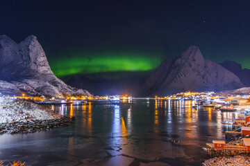 Aurora borealis northern lights over Lofoten Islands, Reine, Hamnoy, Norway, sea rocky shore and fishing villages red rorbu houses