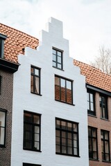 Obraz premium Unique architectural style in a residential neighborhood showcasing a white gabled façade with large windows and traditional roof design in a tranquil urban setting