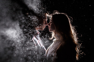 A couple in love stands opposite each other in the rain, raindrops in the backlight. Silhouettes of...