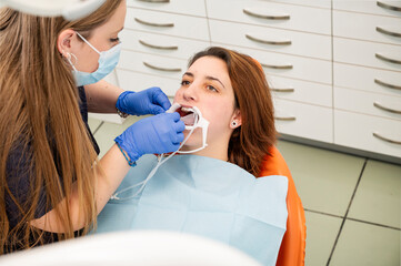 Female dentist in protective mask and gloves performing a dental procedure on a young woman with a...