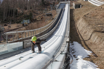 Naklejka premium Ski jumper in the inrun, from the top of the ski jump, skiing down in a crouched position. Slovenia and ski sports destination concepts.