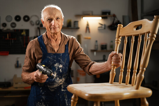 Senior male carpenter restoring old chair for restoration in dark carpentry workshop. Furniture restoration, DIY and hobby