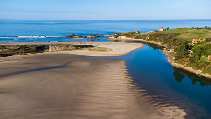 Curving river, sandy La Rabia beach, ocean, and green hills. Cantabria, Spain.