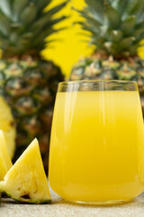 Pineapple juice in a glass among fresh pineapple fruit close-up.
