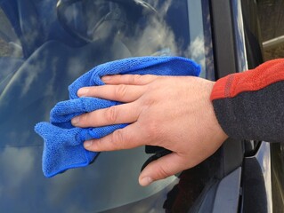 The process of washing car glass by hand with a blue rag. Car care and cleaning.