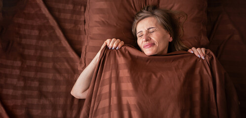 An elderly woman covered with a blanket wakes up in her comfortable bed in the morning smiling...