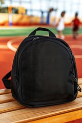 A sleek black backpack rests on a wooden bench, with a blurred playground in the background, suggesting an active, outdoor environment.